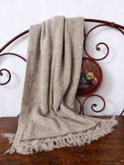 Étole beige en laine d’alpaga à franges, posée sur une tête de lit en fer, sur bois ancien, modèle Kora.